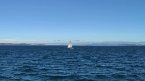 Sailboat-sailing-to-the-Cíes-Islands-alone-with-the-calm-sea-on-a-sunny-day-of-blue-sky-in-the-Rías-Baixas,-shot-blocked-from-the-side,-Pontevedra,-Galicia,-Spain