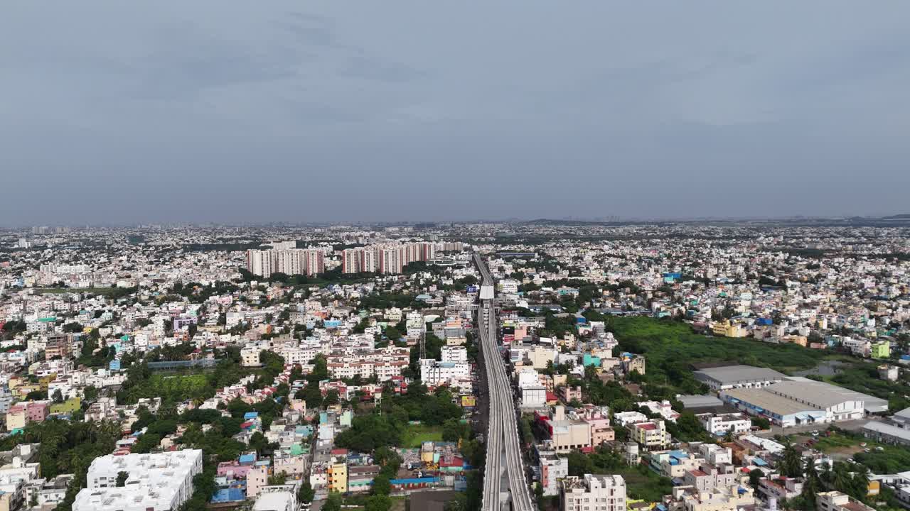 Un'ampia veduta aerea a media altitudine di un ambiente urbano densamente popolato, caratteristico di Chennai. Linea della metropolitana sopraelevata che attraversa il centro dell'inquadratura, dividendo le aree residenziali