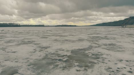 heavy-grey-clouds-above-dirty-brown-frozen-river-surface