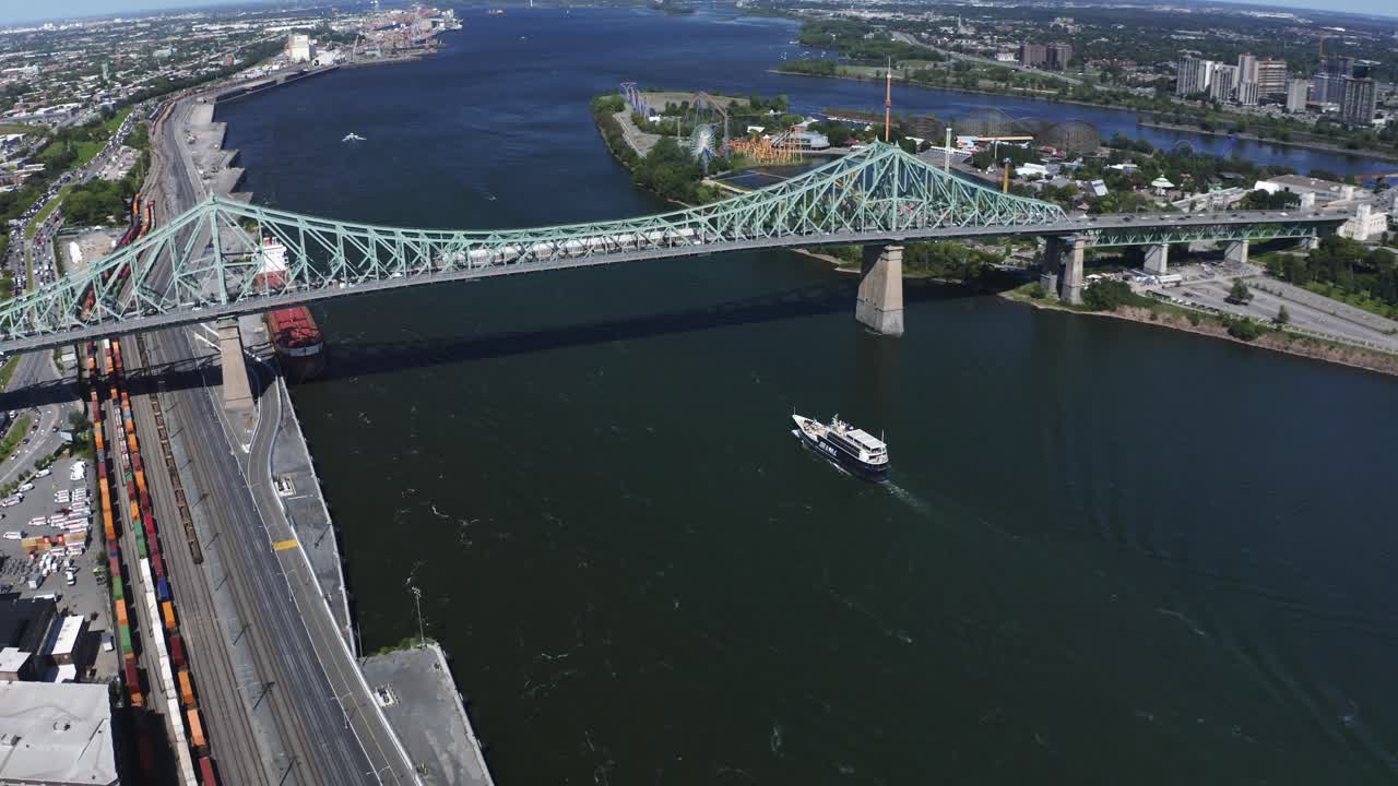 Aerial view of the Jacques Cartier Bridge in Montreal, spanning the St. Lawrence River. Its iconic design and connection between the island and the South Shore, with the city skyline in the backdrop.