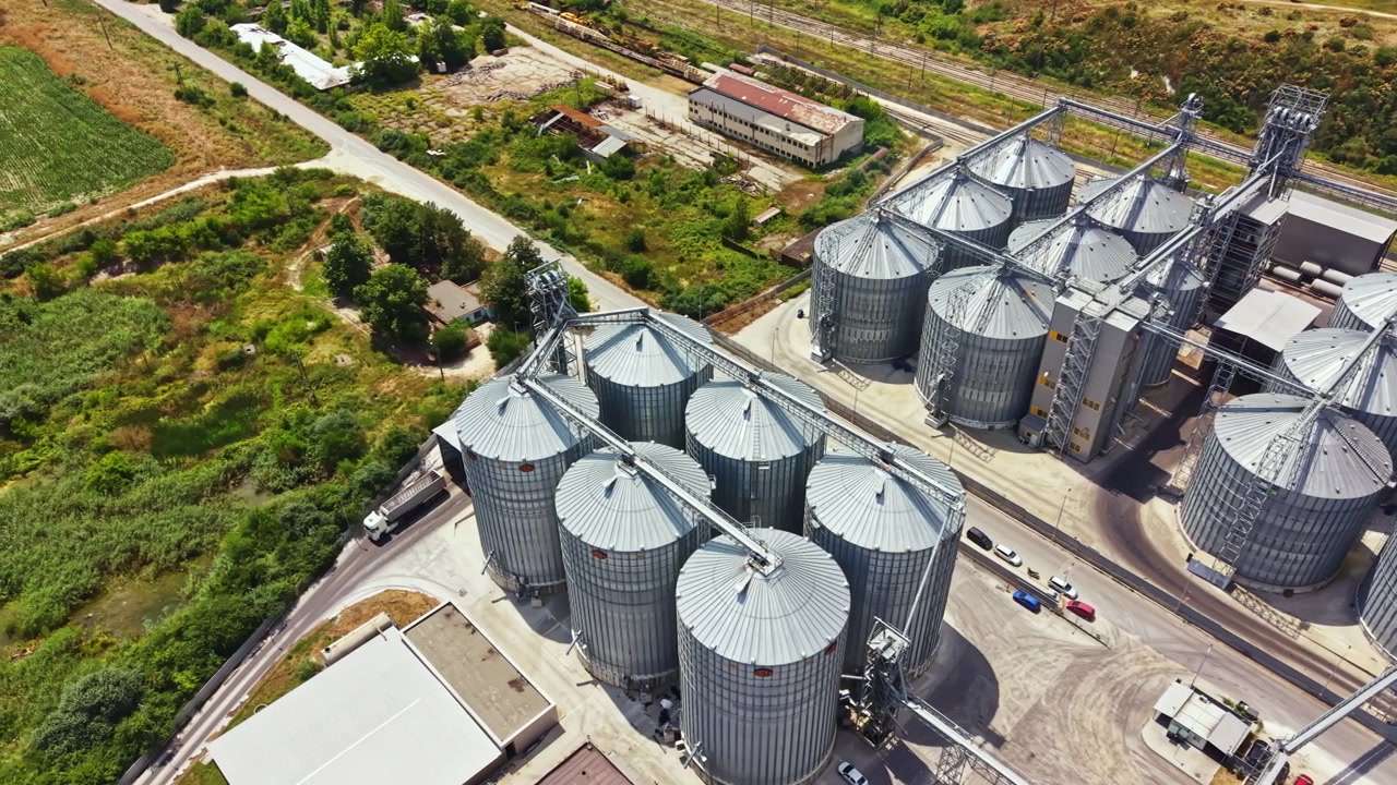 Große Getreidesilos in der Nähe eines Eisenbahngleises in einer ländlichen Gegend mit grünen Feldern im Hintergrund und Zufahrtsstraßen zur Anlage.