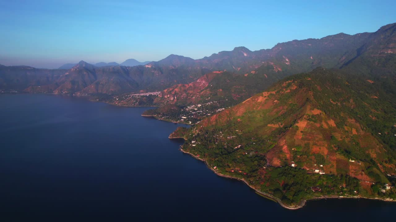 Toàn cảnh từ trên không, lia máy sang phải trên Hồ Atitlan, cho thấy bờ biển gồ ghề, những ngôi làng và ngọn núi trong khung giờ vàng với mặt nước tĩnh lặng và bầu không khí trong lành