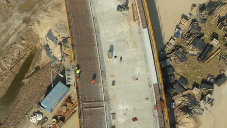 Toma-Panorámica-De-Arriba-Hacia-Abajo-Del-Sitio-De-Construcción-Con-Un-Trabajador,-Construye-Una-Nueva-Carretera-En-Verano