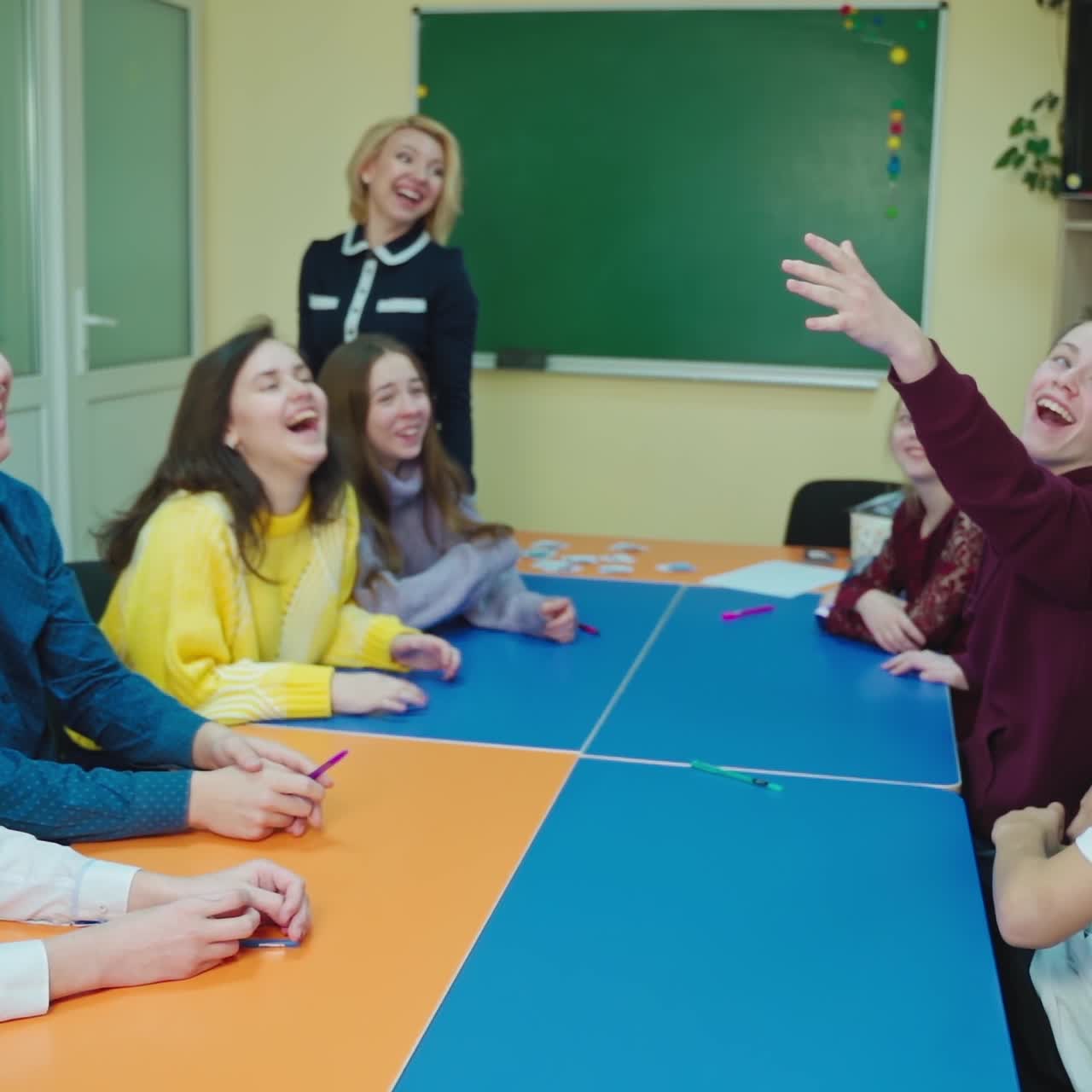Happy students in the classroom. Pupils having fun together at school. Boy is throws up paper and all children laughing. Slow motion.