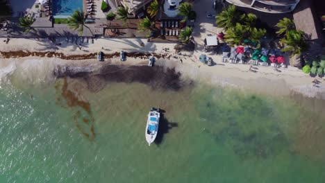 Aerial-view-of-a-solitary-boat-floating-on-crystal-clear-waters-alongside-a-mesmerizingly-beautiful-beach-in-Cancun,-Mexico