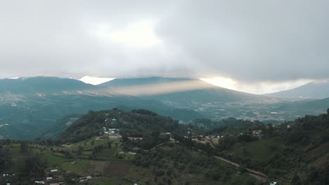 Drone-aerial-view-of-a-beautiful-valley-during-a-cloudy-sunset-with-god-rays,-volcanic-landscape-in-Guatemala