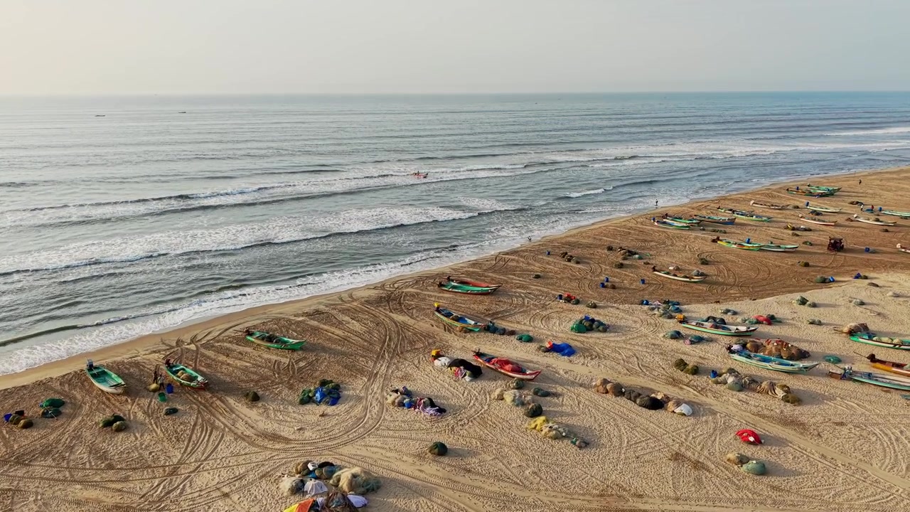 Vista aerea con drone di tradizionali barche da pesca e reti da pesca su una spiaggia sabbiosa a Chennai, accanto al Golfo del Bengala, con dolci onde marine che creano un pacifico scenario costiero mattutino.