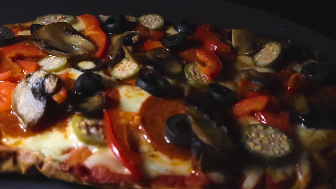 Primo piano di una pizza appena sfornata con salame piccante, mozzarella fusa, olive nere, melanzane e peperoni rossi che ruota lentamente, mettendo in mostra i suoi ingredienti appetitosi e fumanti