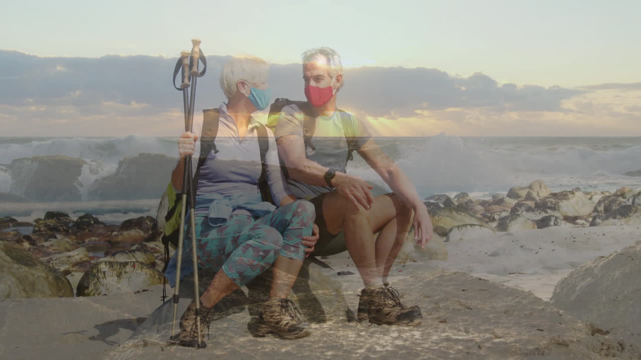 Senior hikers resting on rocky beach at sunset, with animated health graph and weather icons