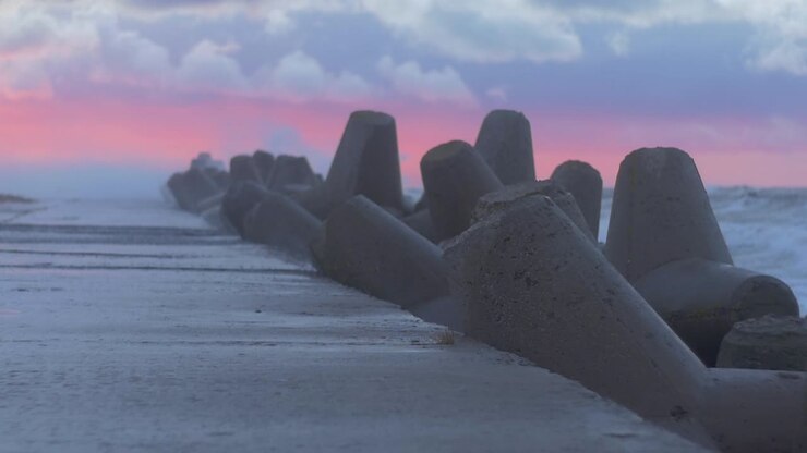Stormfulde havbølger slår mod havnemolen i en farverig solnedgang, slowmotion