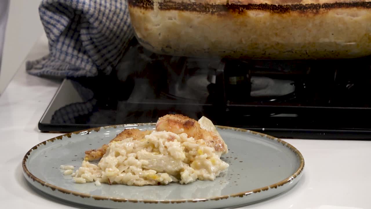 A skilled chef carefully plates a portion of creamy risotto topped with a crispy layer, releasing steam into the air. The dish is served on a simple plate, showcasing its rich texture