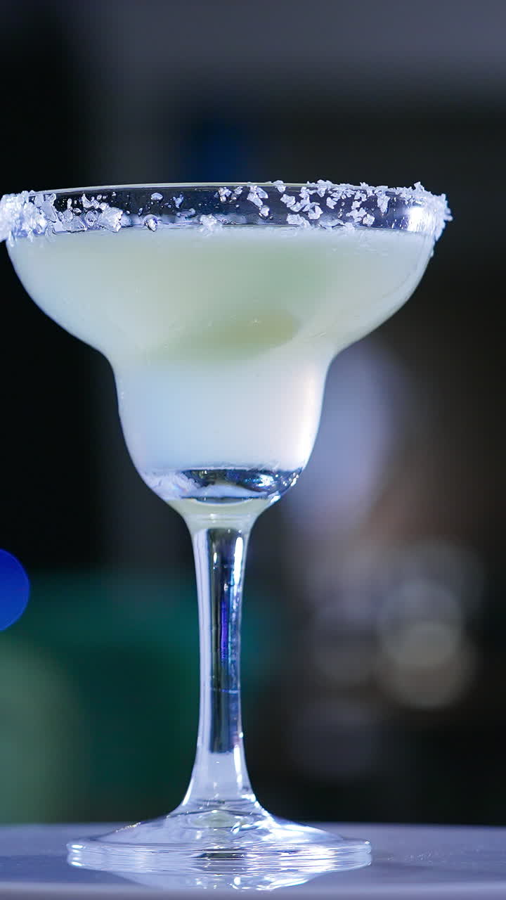 Glass goblet on the little rotating table. Light beverage with a piece of lime inside. Close up. Blurred backdrop. Vertical video