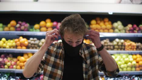 a young man puts on a tissue mask to protect against the epidemic, a close-up portrait. protection from the coronavirus pandemic. standing against grocery shelves