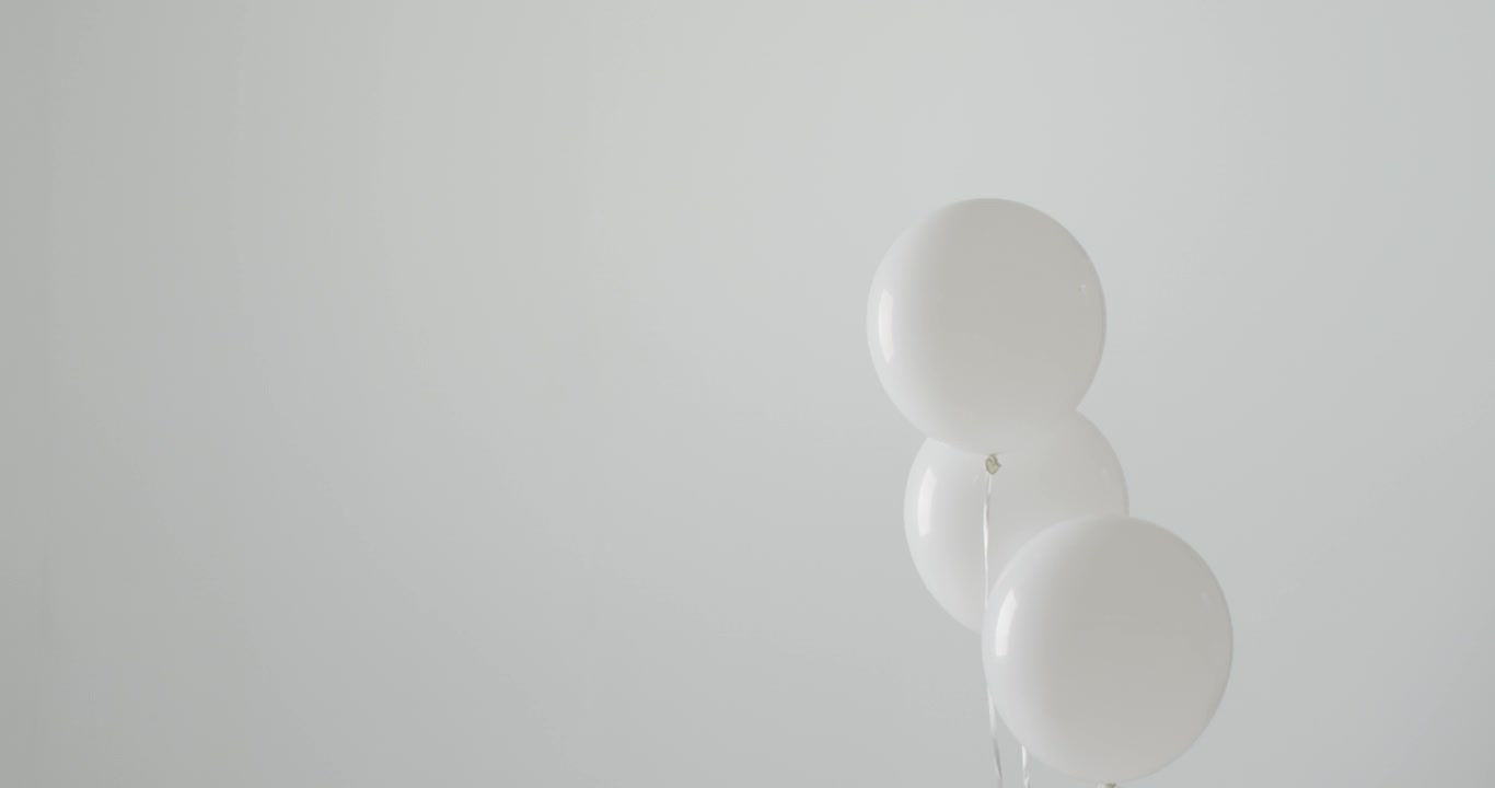 Video von drei weißen Ballons an weißen Schnüren, die auf weißem Hintergrund schweben, mit Textfreiraum