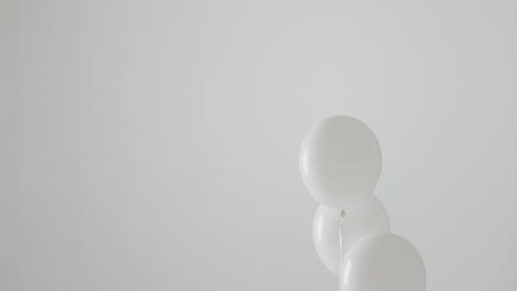 Video-of-three-white-balloons-on-white-strings-floating-on-white-background,-with-copy-space