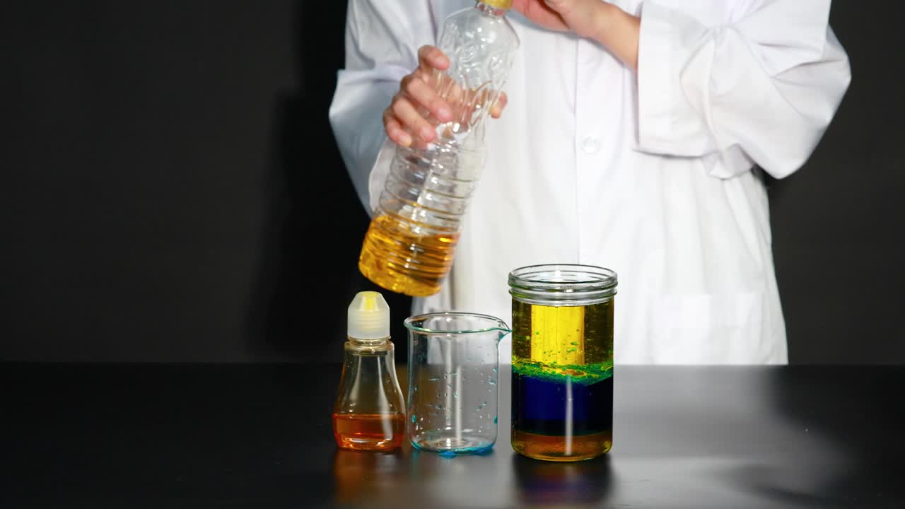 과학자가 액체 밀도 실험을 시연합니다. 다른 액체를 사용하여 항아리에 다채로운 층을 만니다.