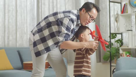 asian father and son playing toy plane together at home