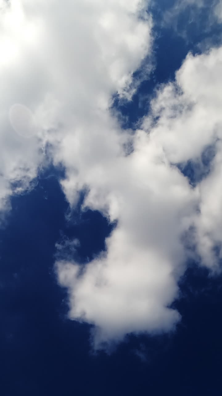 Bright blue summer sky with quickly drifting clouds. White heavy cotton clouds floating blown by the wind. Vertical video