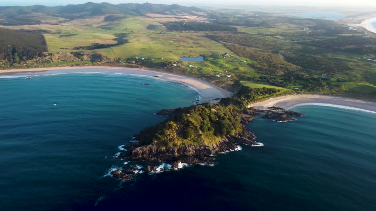 Drone view of beach, bay and grass fields during golden hour sunset at Maitai Bay, Northland, New Zealand.