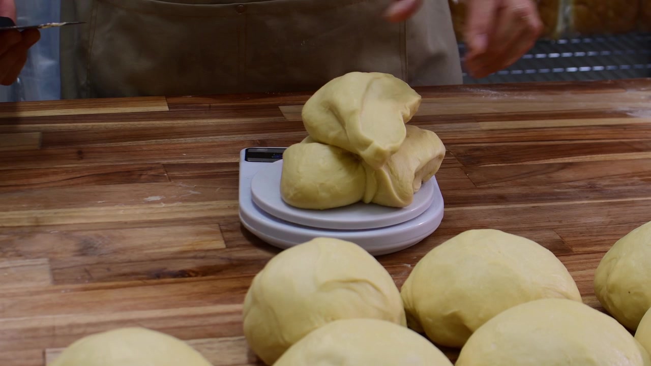 Panettiere divide l'impasto per fare il pane, concentrandosi su precisione e tradizione
