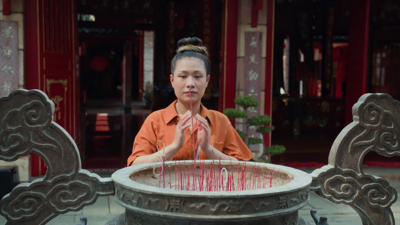 Young Woman Putting Stick in Burner while Praying by Temple