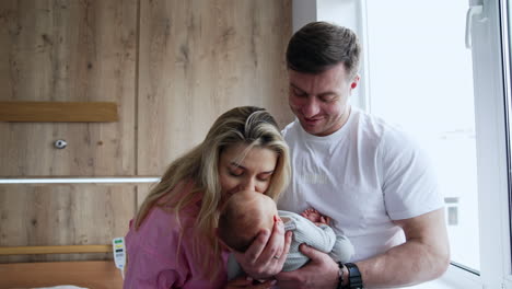 mom and dad with their newborn son in hospital ward. happy parents kissing their beloved baby.