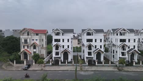 A-newly-constructed-row-of-identical-large-white-multi-story-villa-styled-houses-along-a-suburban-road