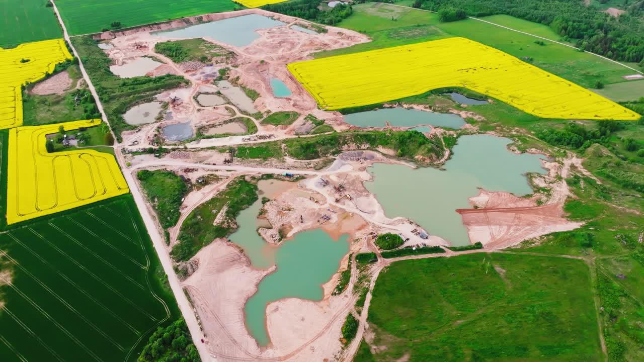 Descending drone focuses on quarry with sandy pools, spring farmland in Latvia