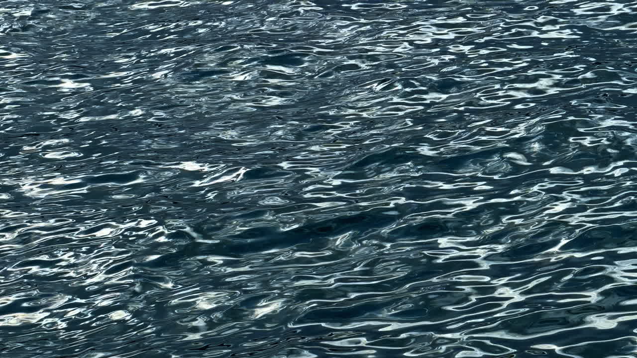 Ondulazioni sulla superficie dell'acqua in pieno giorno in un luogo tranquillo. L'acqua riflette la luce creando increspature durante una giornata di sole in un punto calmo.