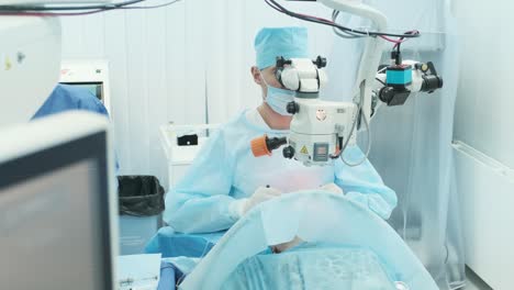 surgeon looking into the microscope at the eye of female patient at the operating room. doctor using microscope during eye surgery process, treatment of cataract and diopter correction.