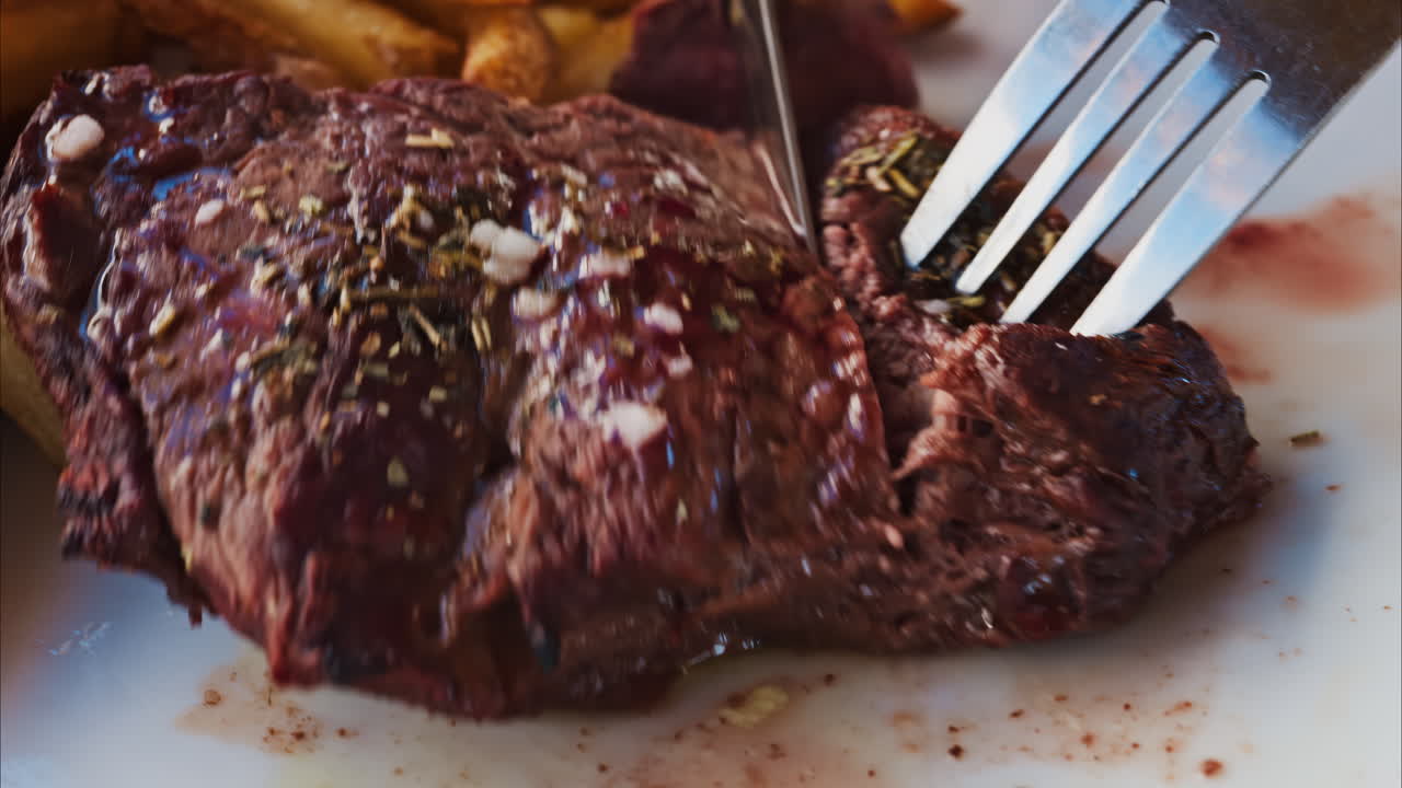 Close up of stake being cut near with fries and salad on a white plate