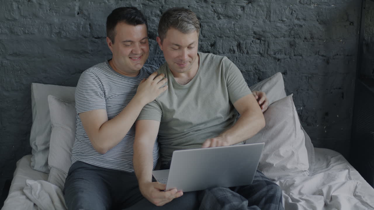 Two men looking at laptop on bed