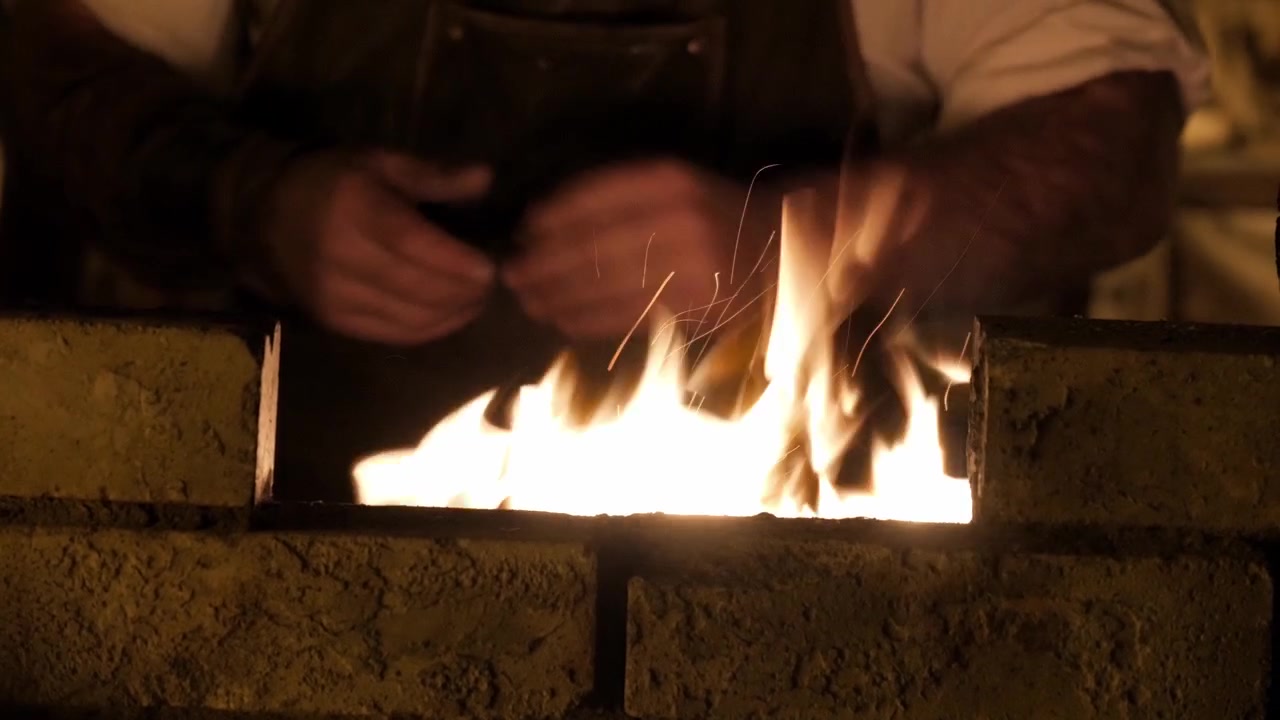 Hands tending a glowing forge fire in a workshop, sparks rising in low light