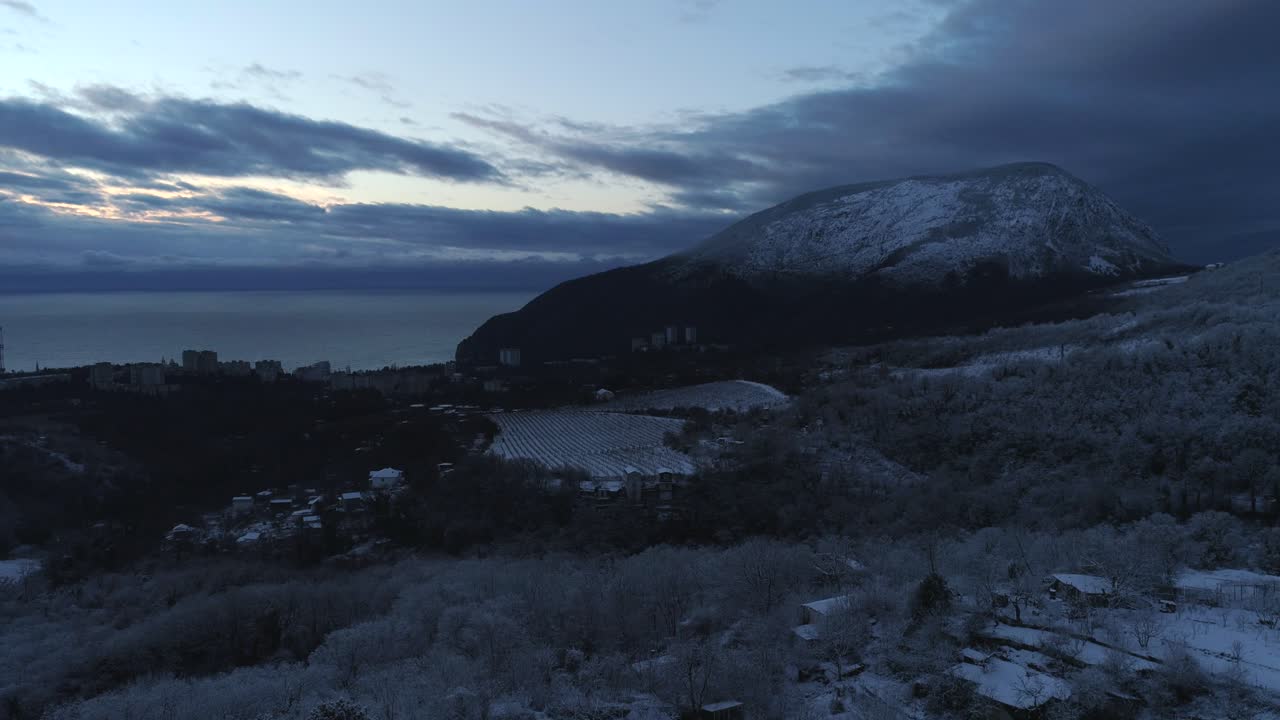 Sneklædt bjerg og kystby ved solopgang/solnedgang