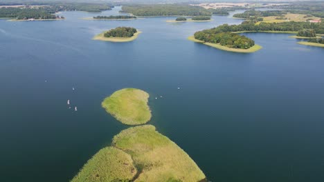 a view of forested islets on the blue waters of the lake with sailboats gliding across