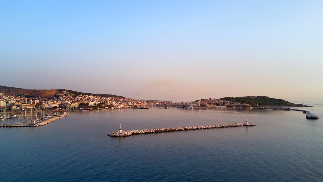 Wide aerial shot gliding towards the port of Mytilene, Lesbos, Greece, featuring boats and the glow of orange sunlight.