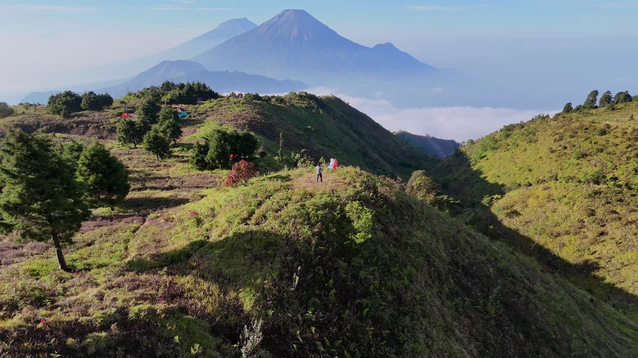 Patriotic moment captured in nature — Aerial view of a hiker raises the Indonesian flag with panoramic view of towering mountain and a sea of clouds on the background