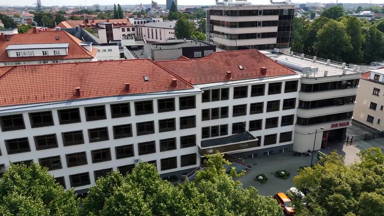L'edificio principale e l'ingresso di emergenza della Respublikinė Klaipėdos ligoninė si ergono sopra le cime degli alberi in un tranquillo movimento di drone diurno.