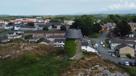 Llangefni-windmill-aerial-view-rising-over-ivy-covered-hillside-landmark-overlooking-Welsh-Snowdonia-mountains,-Anglesey