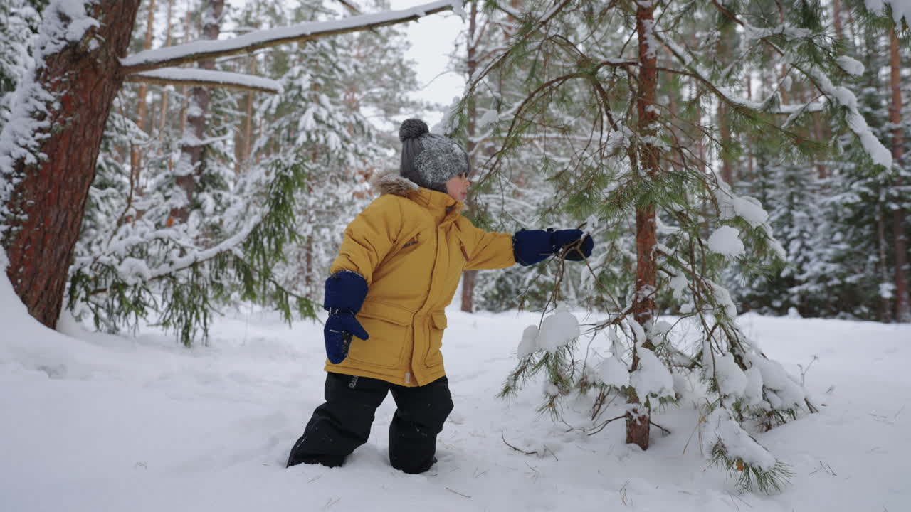 niño pequeño con chaqueta amarilla y sombrero tejido jugando en el bosque en invierno niño está explorando la naturaleza