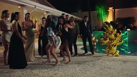 people dancing and socializing at an elegant nighttime pool party