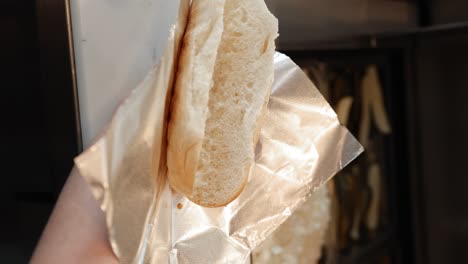 fotografía de cerca de una salchicha asada siendo colocada en un pan de perrito caliente