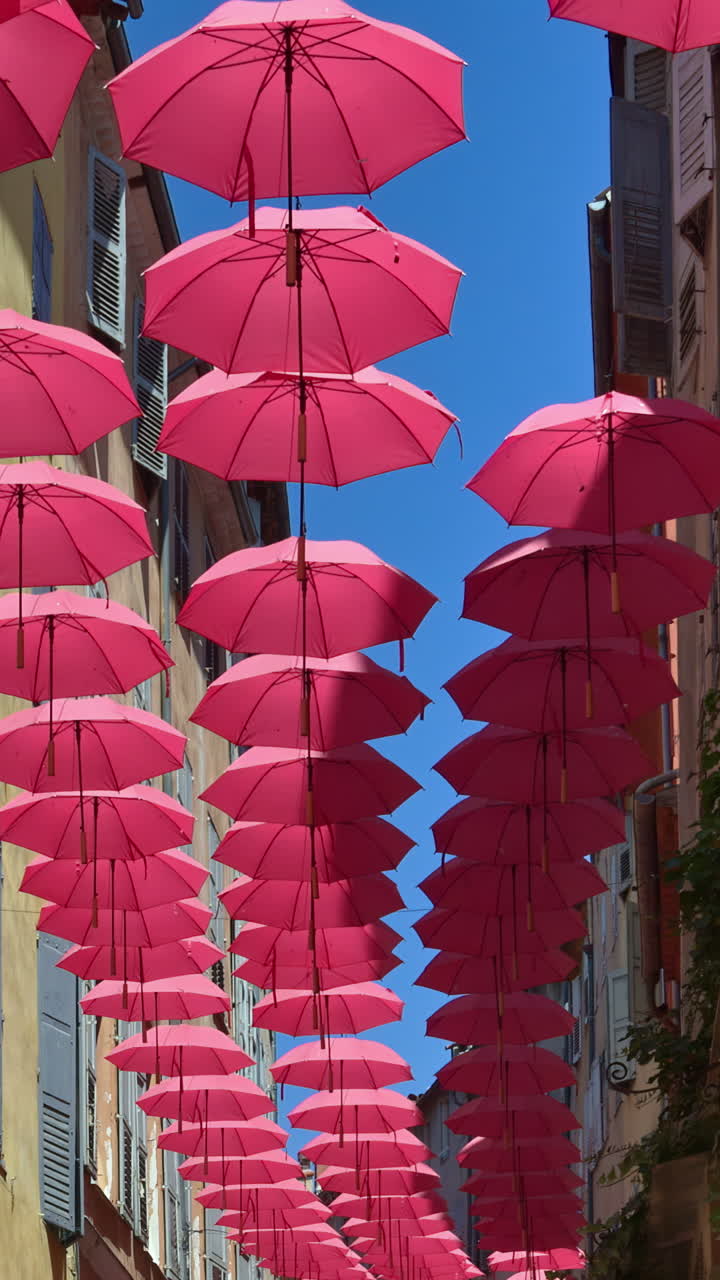 Rows of pink umbrellas above the streets of the old town in Grasse, France with the blue sky on the background. Vertical