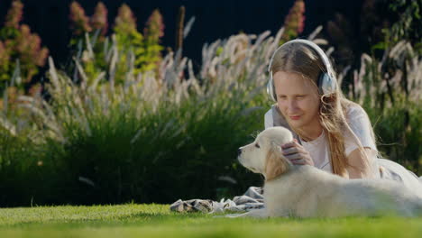 Teenage-girl-plays-with-a-puppy,-lies-on-the-lawn,-listens-to-music-on-headphones