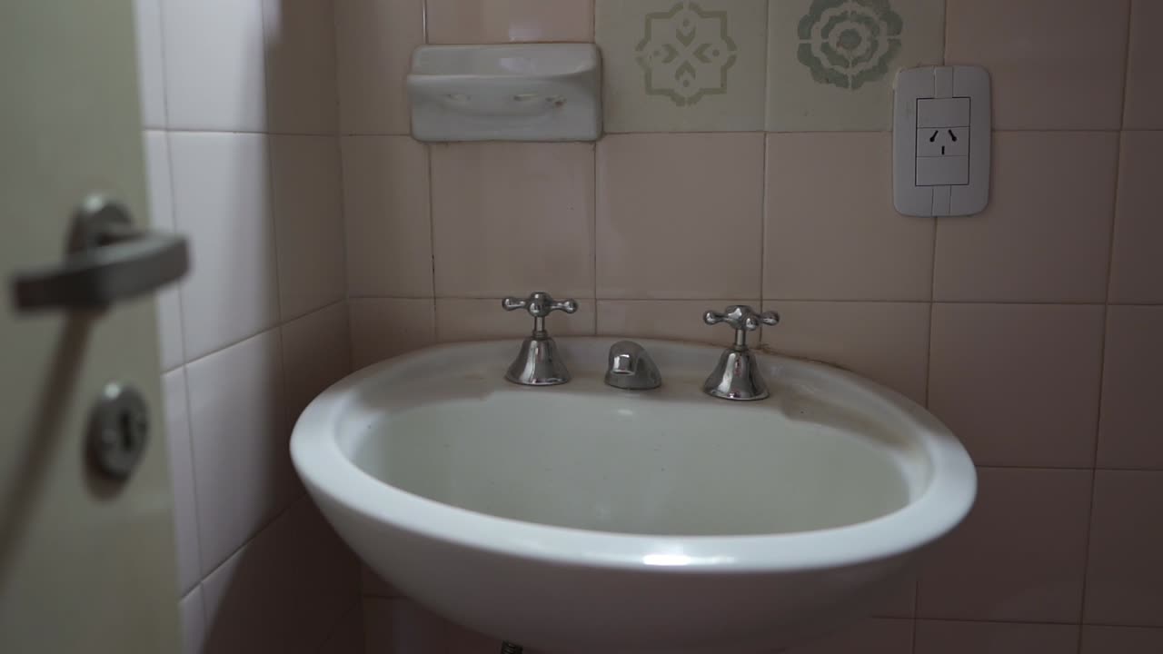 Detailed shot highlights sleek, minimalist metal faucet hardware contrasting with soft pink-white tiled wall. Perfect for modern rental listings.