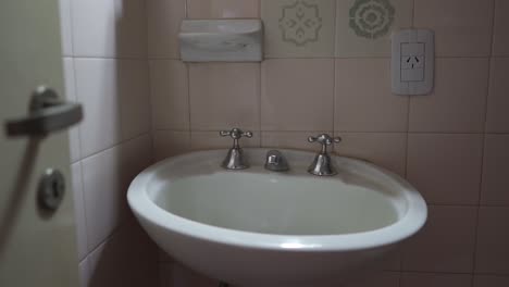detailed shot highlights sleek, minimalist metal faucet hardware contrasting with soft pink-white tiled wall. perfect for modern rental listings.