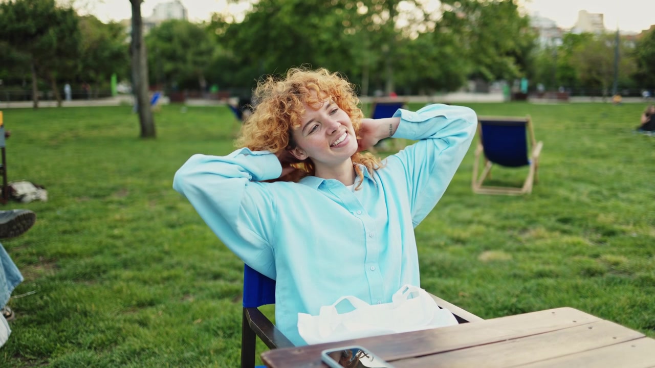 Giovane donna felice con capelli rossi ricci che si rilassa in un parco.