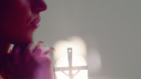 praying with hands clasped, person in soft light with illuminated cross