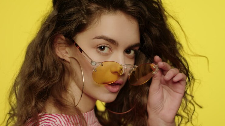 Woman in yellow glasses looking to camera and winking eye in studio
