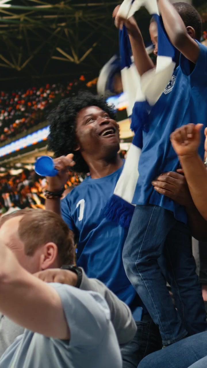Video Vertical Padre afroamericano con vuvuzela celebrando con su hijo pequeño en un estadio de fútbol